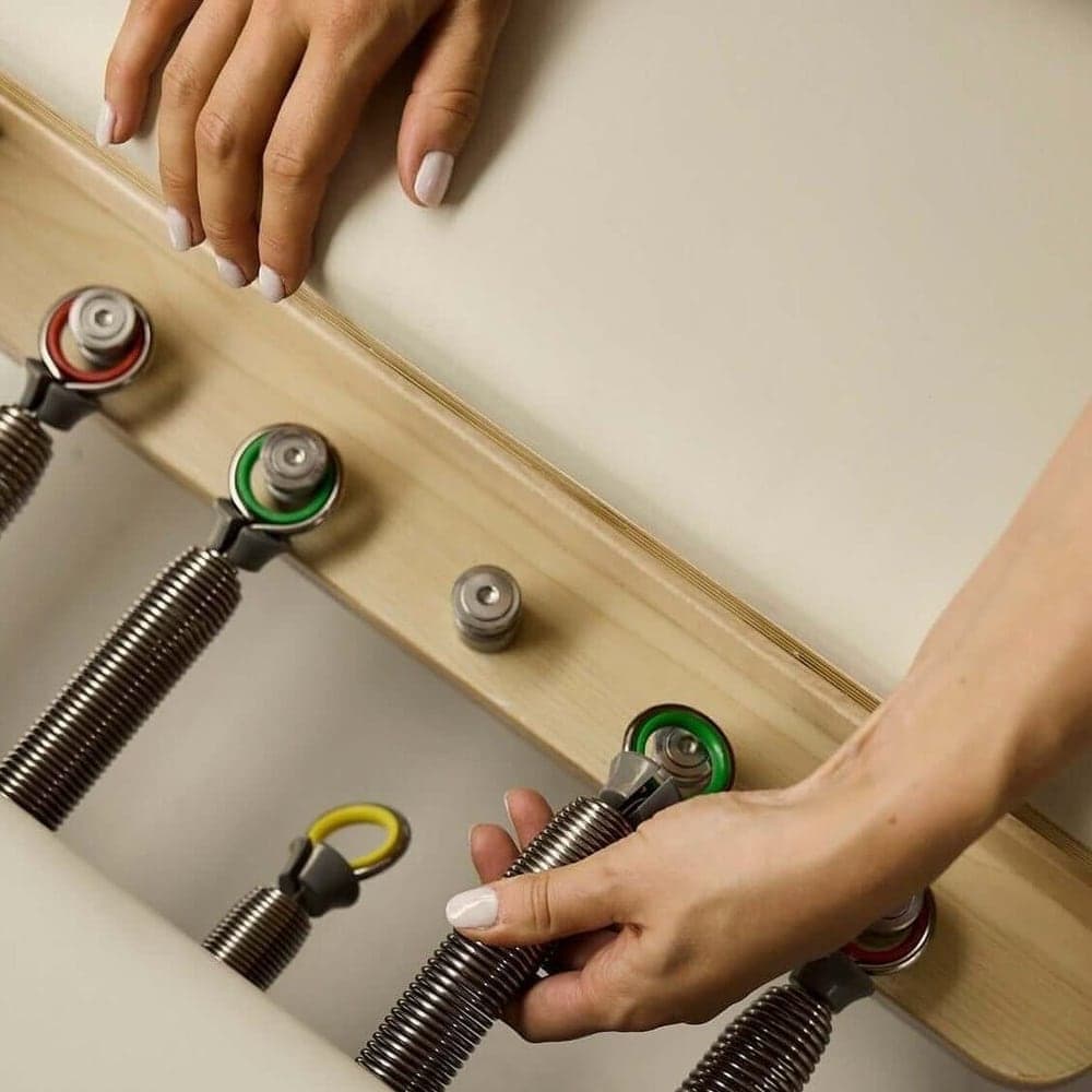 Primer plano de los muelles de colores de una cama reformer, y una mano ajustando la resistencia